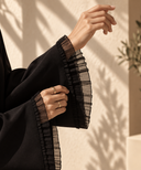 Black ruffle trim abaya with sheer ruffle cuff detail in soft natural light