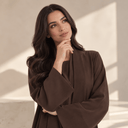 Woman in a brown abaya thoughtfully resting her hand on her chin while choosing the right abaya style