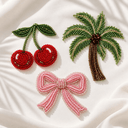 Beaded cherry, palm tree and pink bow embroidery motifs on ivory fabric, inspired by whimsical abaya cuff details.