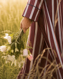 Close-up of a woman in a burgundy and navy striped abaya holding a bouquet of white lilies and pink tulips in a golden field
