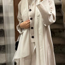 Person wearing a white coat with black buttons in an outdoor setting.