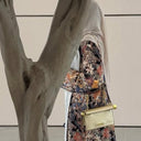Person wearing a floral dress holding a gold handbag against a neutral background