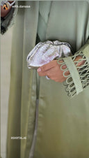 Hand holding a silver clutch with a person wearing a light green outfit in the background