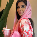 Woman wearing a pink hijab and floral dress holding a pink cup with a straw.