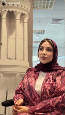 Woman in a patterned outfit sitting in an indoor setting with architectural elements.