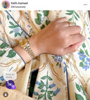 Hand wearing a gold watch and ring on a floral-patterned fabric background